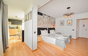 A modern bedroom with a large bed, a headboard with a brick pattern, and a dining area in the background. - One by One - Adam's Studio - Cismigiu Gardens (Bucharest)
