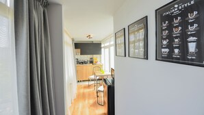 A modern kitchen with wooden cabinets, a dining area with a table and chairs, and a kitchen island. There are framed pictures on the wall, including one with coffee cup designs. - One by One - Adam's Studio - Cismigiu Gardens (Bucharest)