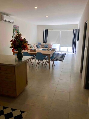 A modern living room with a sofa, a dining table with chairs, and a kitchen area with a counter and cabinets.