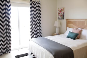 A bedroom with a bed, a nightstand, a lamp, and a window with curtains. - Beautiful Condo 300 Meters To Medano Beach (Cabo San Lucas)