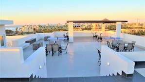 A rooftop terrace with seating areas, a covered section, and a view of the cityscape and beach. - Beautiful Condo 300 Meters To Medano Beach (Cabo San Lucas)