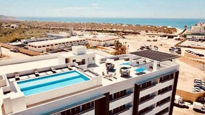 A modern hotel with a rooftop pool, multiple floors, and a view of the beach and ocean. - Beautiful Condo 300 Meters To Medano Beach (Cabo San Lucas)
