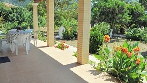 Eine Terrasse im Freien mit Tisch und Stühlen, umgeben von Pflanzen und Blumen.