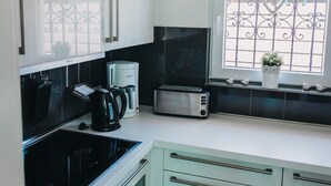 A modern kitchen with white cabinets, a black stove, a coffee maker, and a window with decorative bars. - Holiday Home 'Haus Piratennest' with Private Terrace, Garden & Wi-Fi (Grömitz)