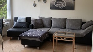 A living room with a sofa, a chair, a glass coffee table, and wall art. - Holiday Home 'Haus Piratennest' with Private Terrace, Garden & Wi-Fi (Grömitz)