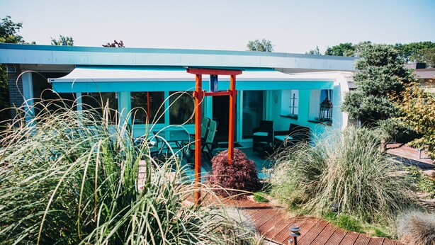 A modern building with a blue exterior, a red entrance, and a patio area with plants. - Holiday Home 'Haus Piratennest' with Private Terrace, Garden & Wi-Fi (Grömitz)