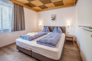 A bedroom with a bed, two bedside tables, a window with curtains, a wall-mounted light, and a radiator.