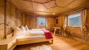 Quarto de madeira com uma cama, uma mesinha e uma janela com cortinas.