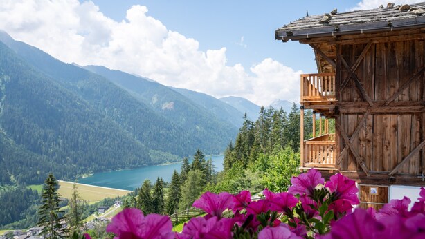 Uma cabana de madeira com varanda com vista para um lago e montanhas.