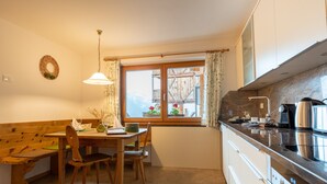Uma cozinha com um banco de madeira, uma mesa de jantar e uma janela com vista para um deck de madeira e flores.