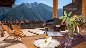 Mesa de jantar com um prato de comida, uma churrasqueira e vista para montanhas.