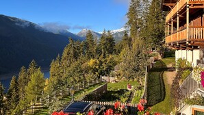 Uma pousada de montanha com varanda de madeira, um jardim florido e vista para montanhas nevadas.