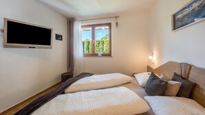 A bedroom with two beds, a TV, a window with a view, and a painting on the wall.