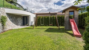 A backyard with a wooden playhouse, a red slide, and a swing set.