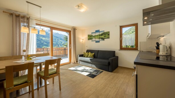 A modern living room with a dining area, a sofa, a coffee machine, and a view of mountains through the windows.