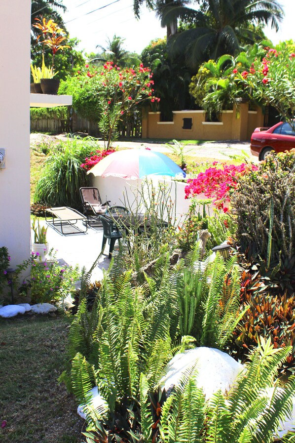 Un jardín con plantas en macetas, una mesa con sillas y un coche rojo aparcado cerca.