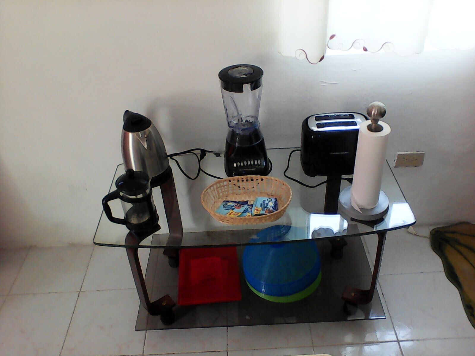 A glass-top table with a blender, toaster, and a basket of snacks.