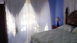 Une chambre à coucher avec un lit, un ventilateur de plafond, un climatiseur et des rideaux.