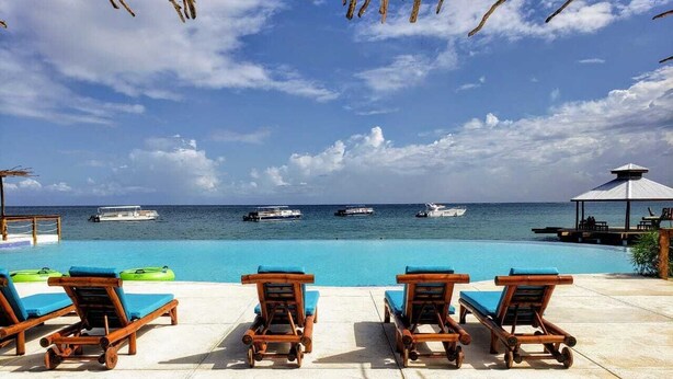 Un espace aménagé au bord de la piscine, avec des chaises longues en bois et une vue sur l’océan.