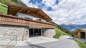 Een berghut met een gevel van natuursteen, een houten balkon en een garage-ingang.