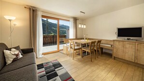 Een moderne woonkamer met een bank, een eettafel met stoelen, een televisie en uitzicht op de omgeving.