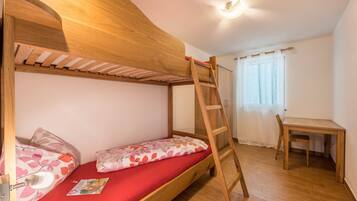 Een stapelbed met een ladder, een klein bureau en een stoel in een kamer met houten vloer en witte wanden.