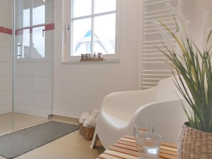 Een moderne badkamer met een glazen douche, een witte badkuip, een raam met uitzicht en een rieten mand met handdoeken.