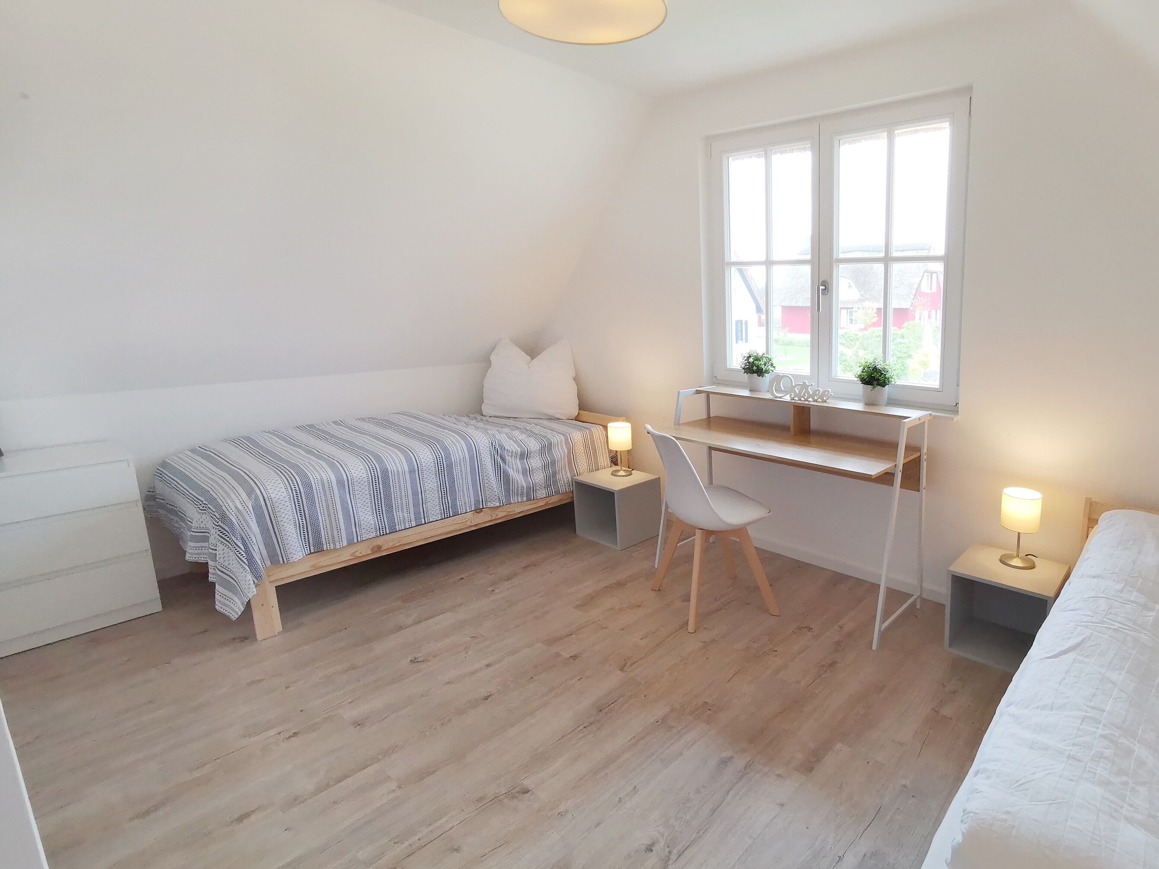 Ein Schlafzimmer mit Bett, Schreibtisch, Stuhl, Fenster und Nachttischlampen.