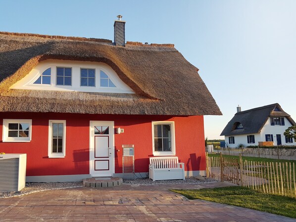 Een rood huis met rieten dak, witte ramen en een schoorsteen.