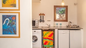 A compact kitchen with a washing machine, a dishwasher, a microwave, and a window with a view of greenery.
