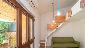 A room with a green sofa, a wooden staircase, and a window with a view of greenery.