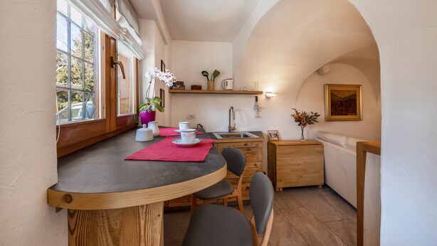 A compact kitchen with a dining area, wooden cabinets, a sink, and a window with a view. - Apartment "Mariagrazia" with Mountain Views and Garden (Tesero)