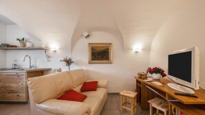 A cozy living room with a sofa, a small table, a TV, and a kitchen area in the background. - Apartment "Mariagrazia" with Mountain Views and Garden (Tesero)