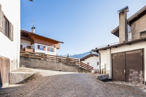 A cobblestone street leading to a building with a wooden balcony and a mountain backdrop.