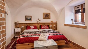 A bedroom with a wooden bed, a nightstand, a dresser, a window with a view, and a ceiling light. - Apartment "Mariagrazia" with Mountain Views and Garden (Tesero)