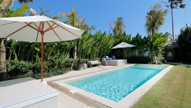 Una piscina circondata da vegetazione lussureggiante, con zona relax e un ampio ombrellone che offre ombra.