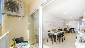 A modern apartment with a dining area, kitchen, and a balcony with an air conditioning unit. - Summer Breeze Comfort Apartment (Mellieha)