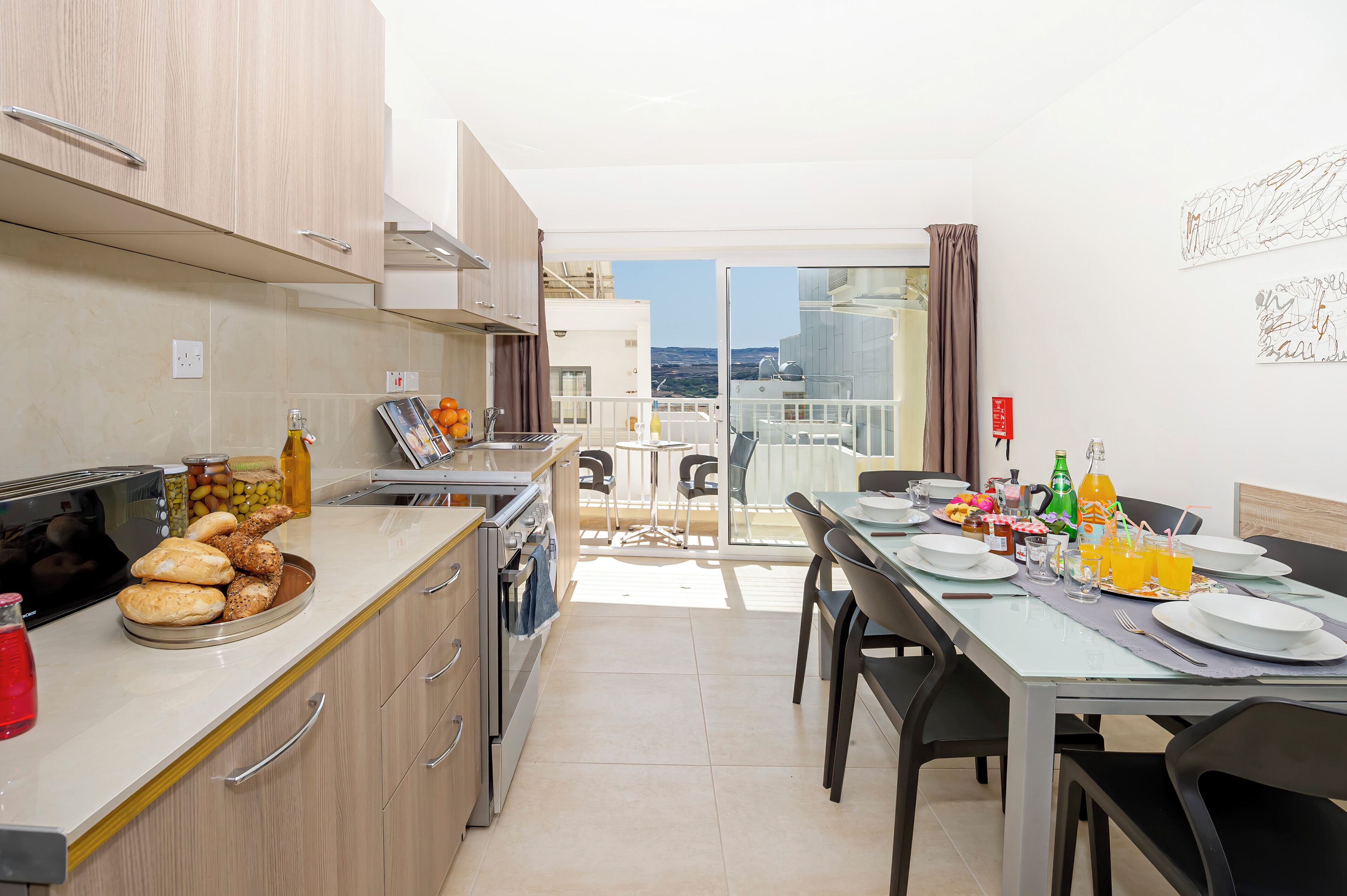 A modern kitchen with a dining area, featuring a balcony with a city view.