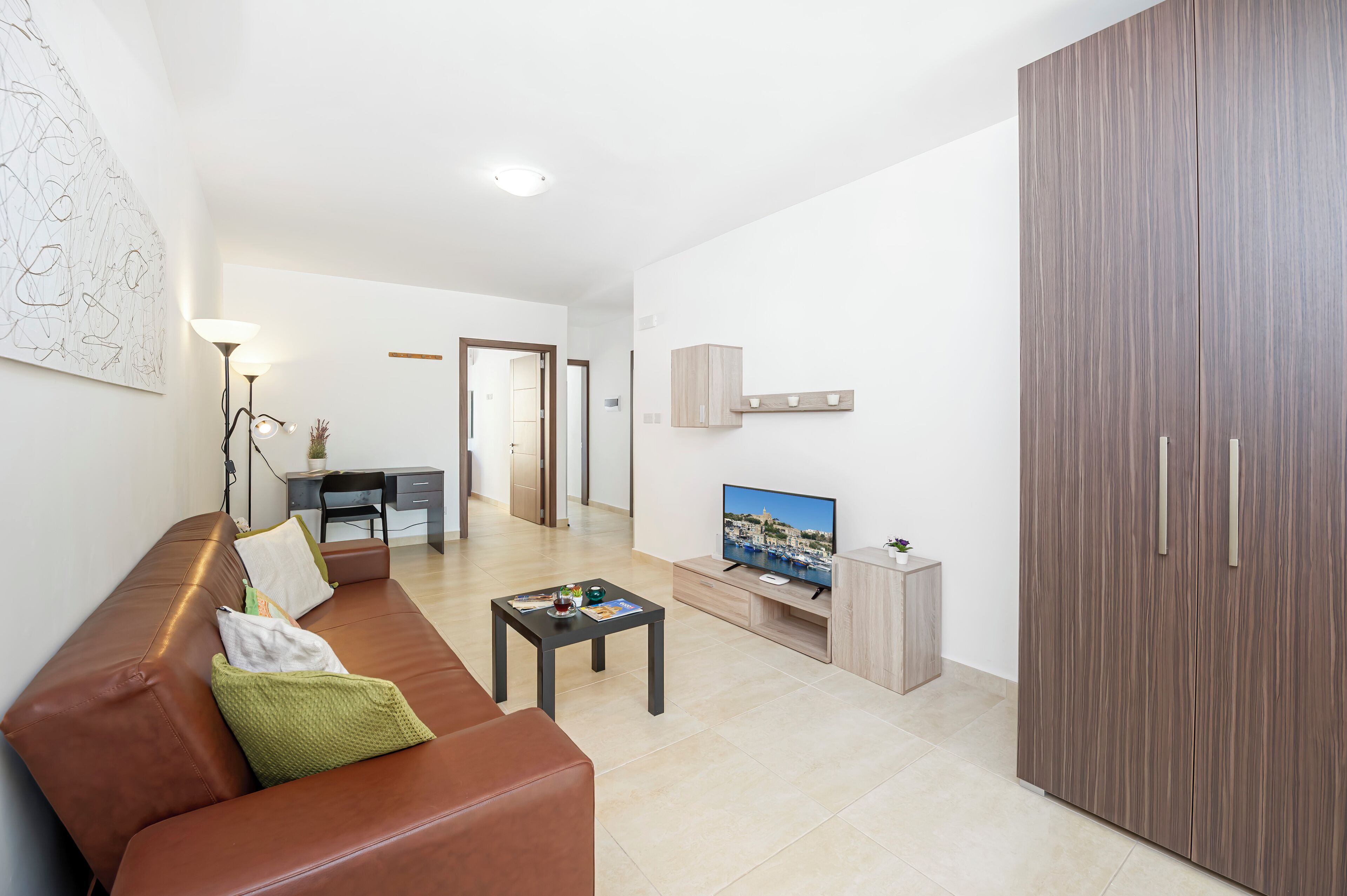 Una sala moderna con un sofá de cuero marrón, una mesita de centro, un televisor sobre un mueble bajo y un armario.