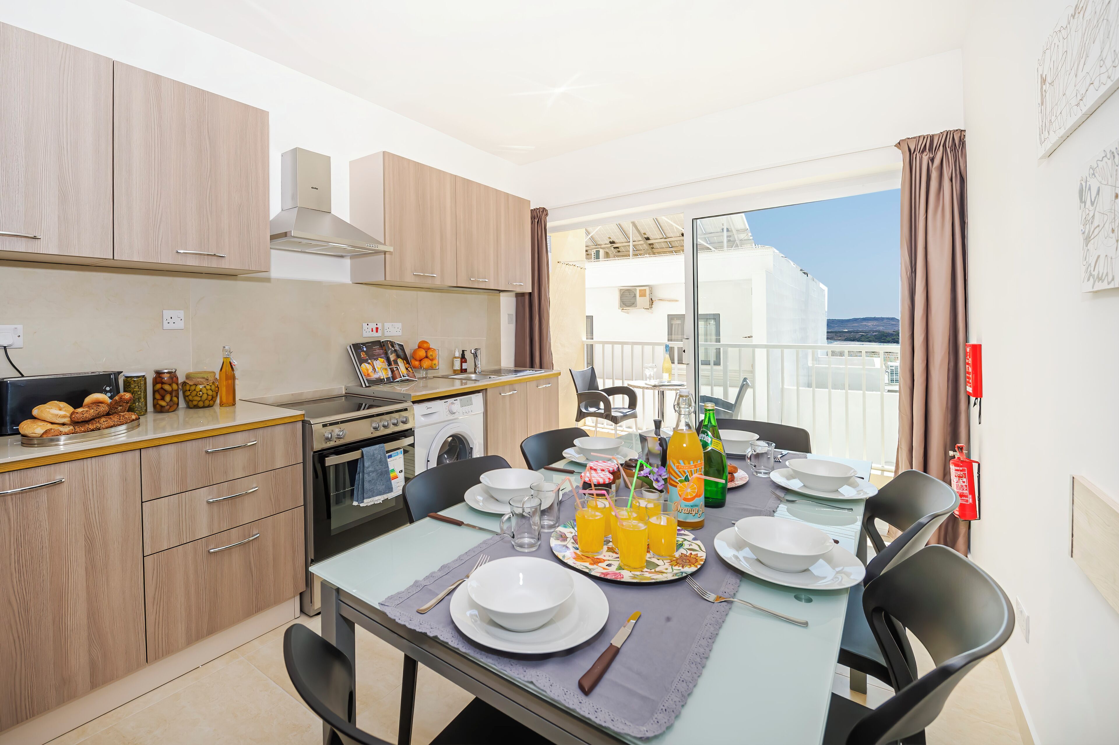 Una cocina moderna con armarios de madera, una mesa de comedor con platos, vasos y una botella de jugo de naranja.
