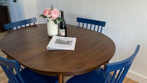 Una mesa redonda de madera para comer con cuatro sillas azules, un jarrón con flores, una botella y un menú sobre la mesa.