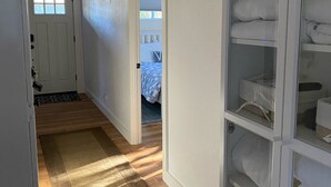 Un pasillo con suelo de madera, un tapete marrón, una puerta blanca y un armario con estantes.