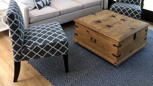 Una sala de estar con un sofá color beige, sillones estampados, una mesa de centro de madera y un cuadro grande de un paisaje en la pared.
