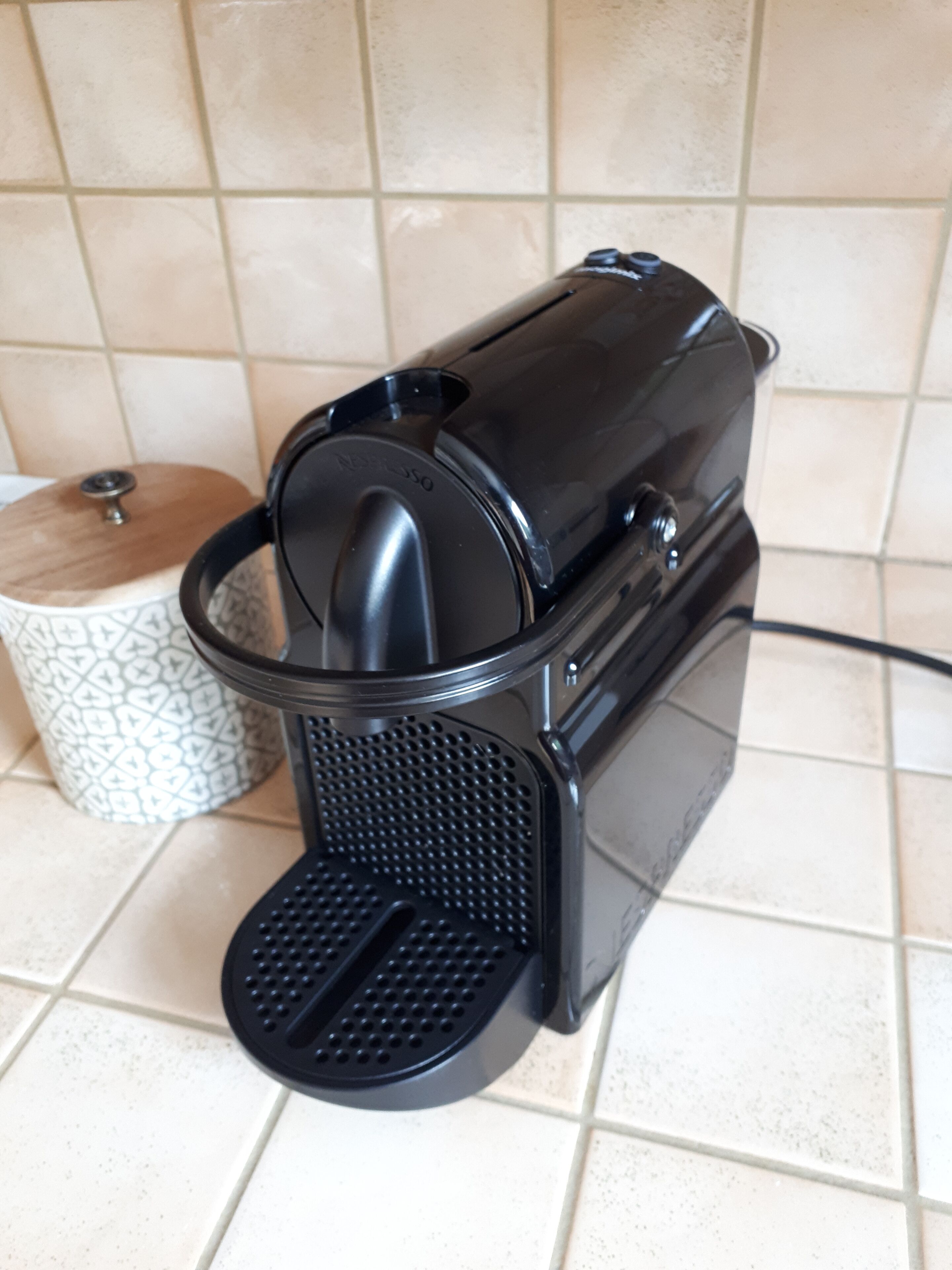 Een koffiezetapparaat met een zwart voetstuk en een transparante waterreservoir, staand op een betegelde vloer.