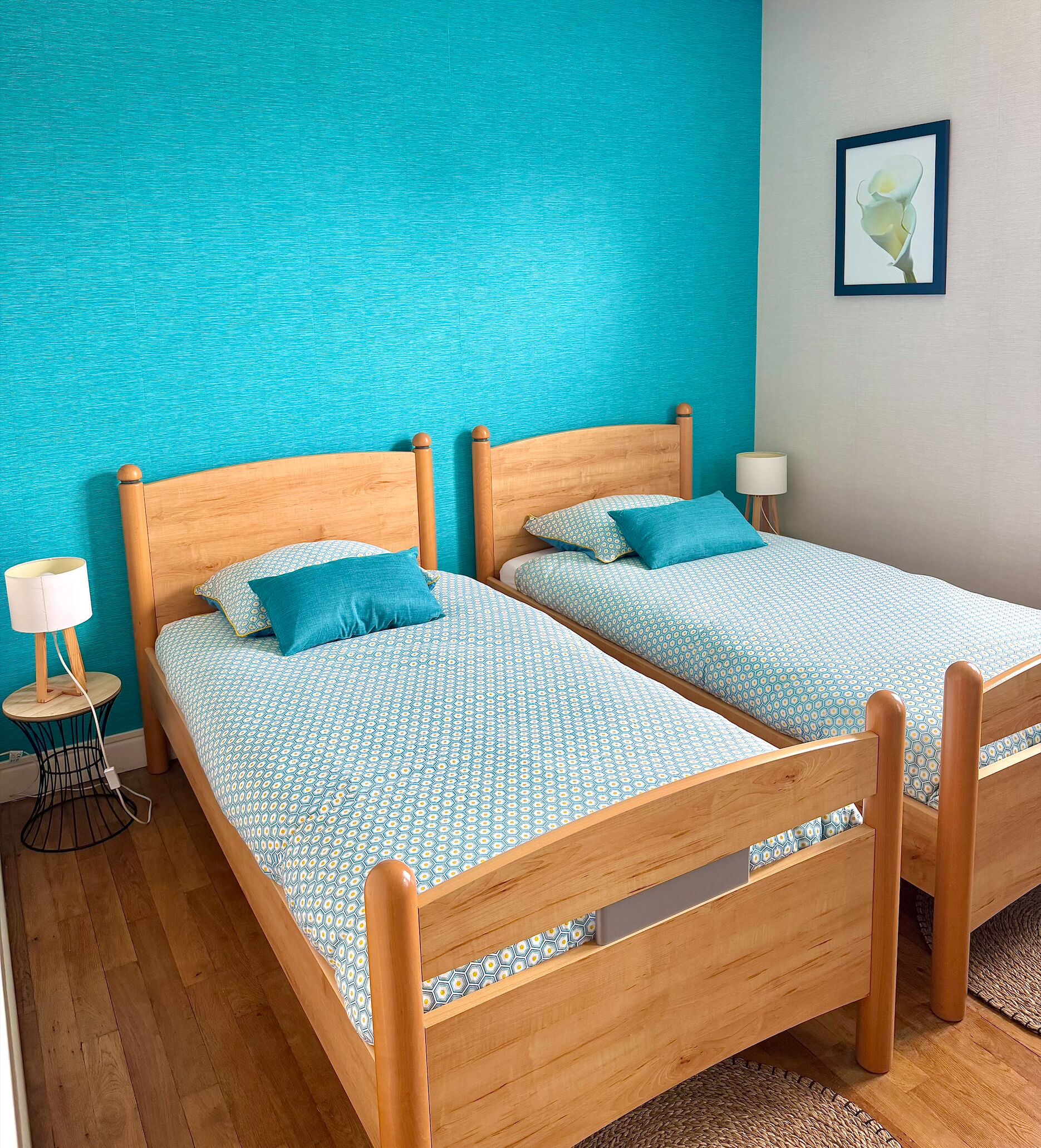 Un lit double avec une couvre-lit à motifs, une table de chevet avec une lampe et un mur orné d’un tableau encadré.