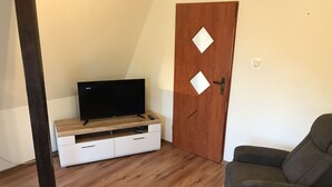A living room with a flat-screen TV on a wooden TV stand, a grey sofa, and a wooden door with diamond-shaped cutouts.