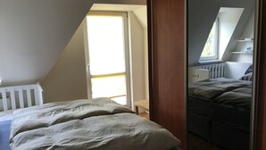 A bedroom with a sloped ceiling, a bed with white bedding, a small bedside table, and a window with a view of the outside.