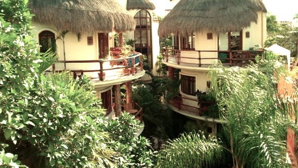 A resort with thatched-roof buildings, balconies, and lush greenery. - One Bedroom Apt In The Heart Of Playa Only One Block to the Beach! (Playa del Carmen)