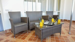 Una habitación con mobiliario de mimbre, una mesa de cristal con un ordenador portátil y bebidas, y suelo de baldosas.
