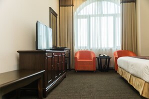 A hotel room with a bed, a desk, a television, and two armchairs.